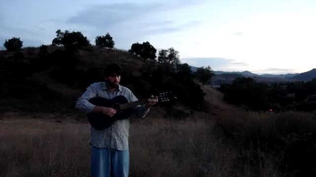 Daniel standing in a field with his guitar at dusk